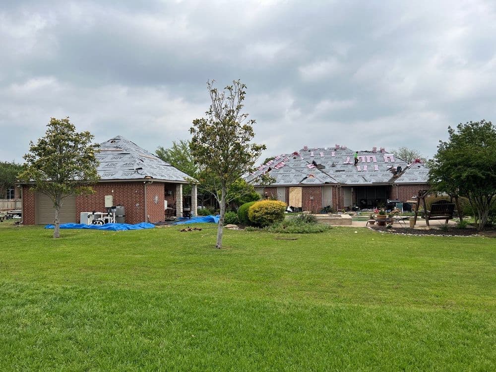 Houses under roof renovation surrounded by green lawn and trees on overcast day.
