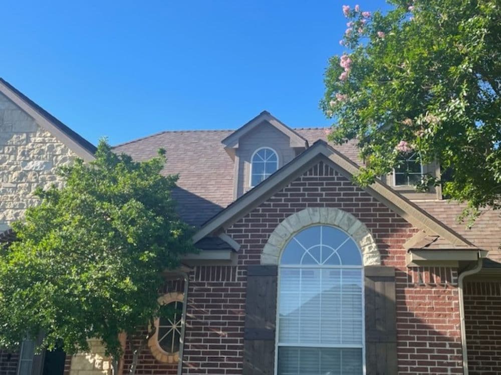 Brick house with arched window, lush green tree, and clear blue sky in the background.