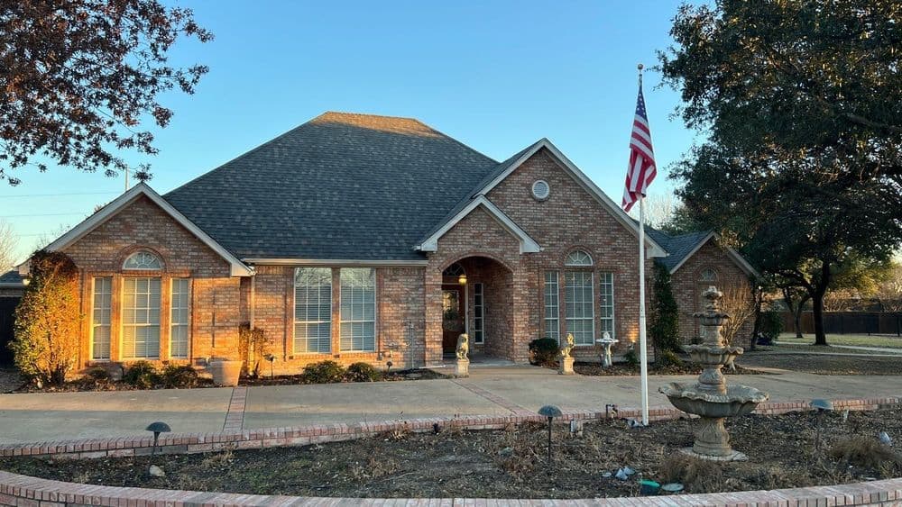 Brick house with American flag, landscaped yard, and elegant fountains in front.