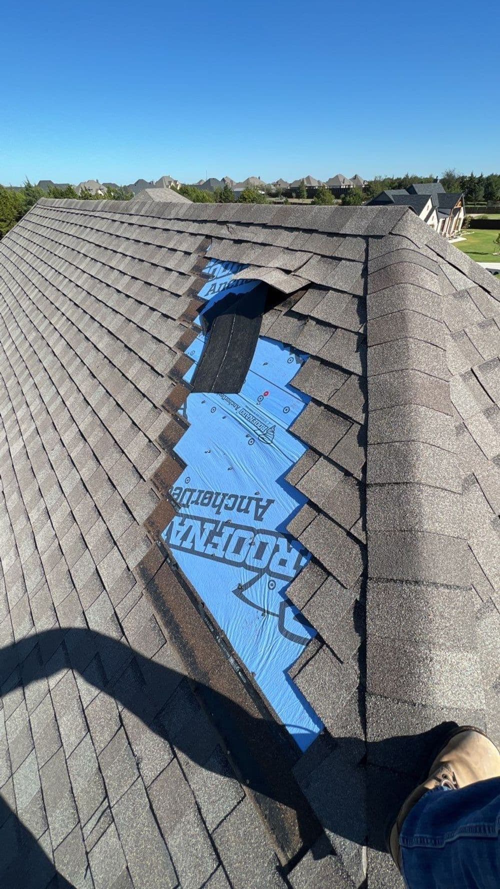 Roof with missing shingles, exposing underlayment and repair area on a sunny day.