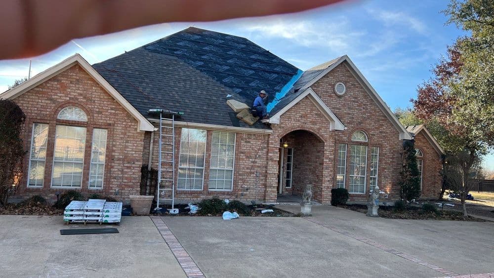 Man installing new shingles on a brick house roof under blue sky. Construction, home improvement.