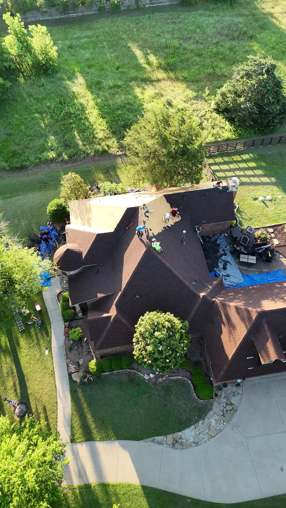 Aerial view of a house with a roof renovation in progress surrounded by greenery.