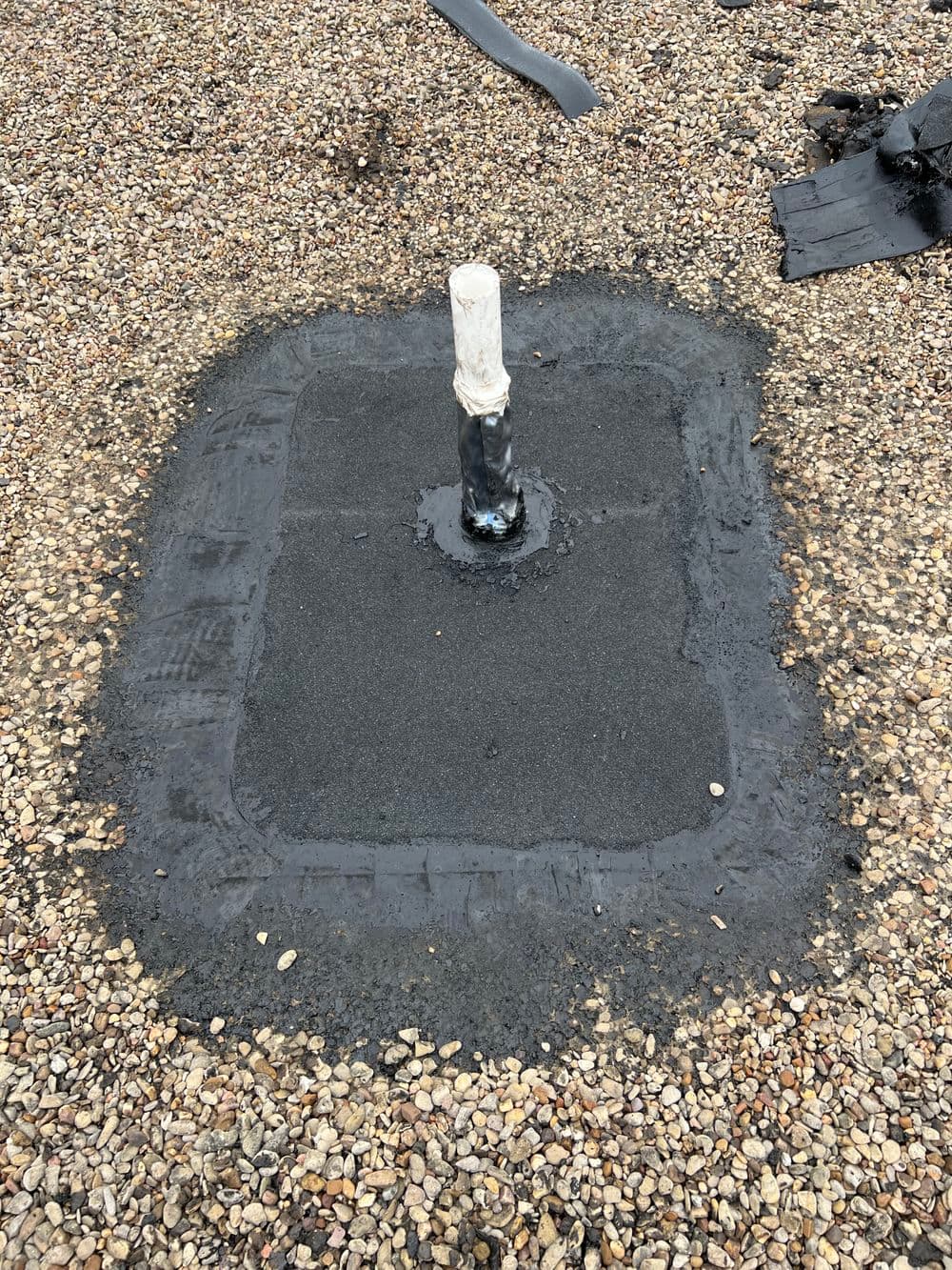 Roofing repair with sealed vent pipe on gravel surface, showcasing durable waterproofing.