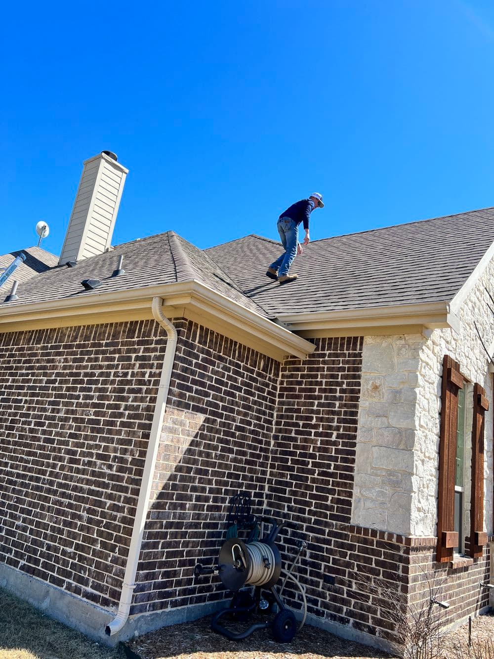 Worker inspecting a residential roof under clear blue skies.