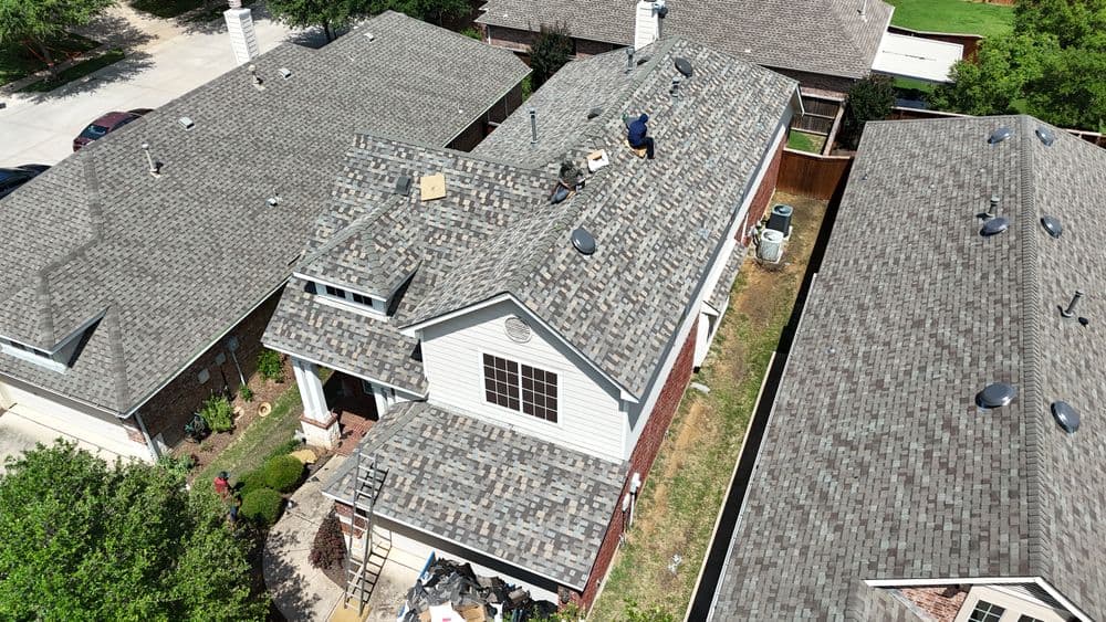 Aerial view of a worker repairing a shingle roof on a suburban home.