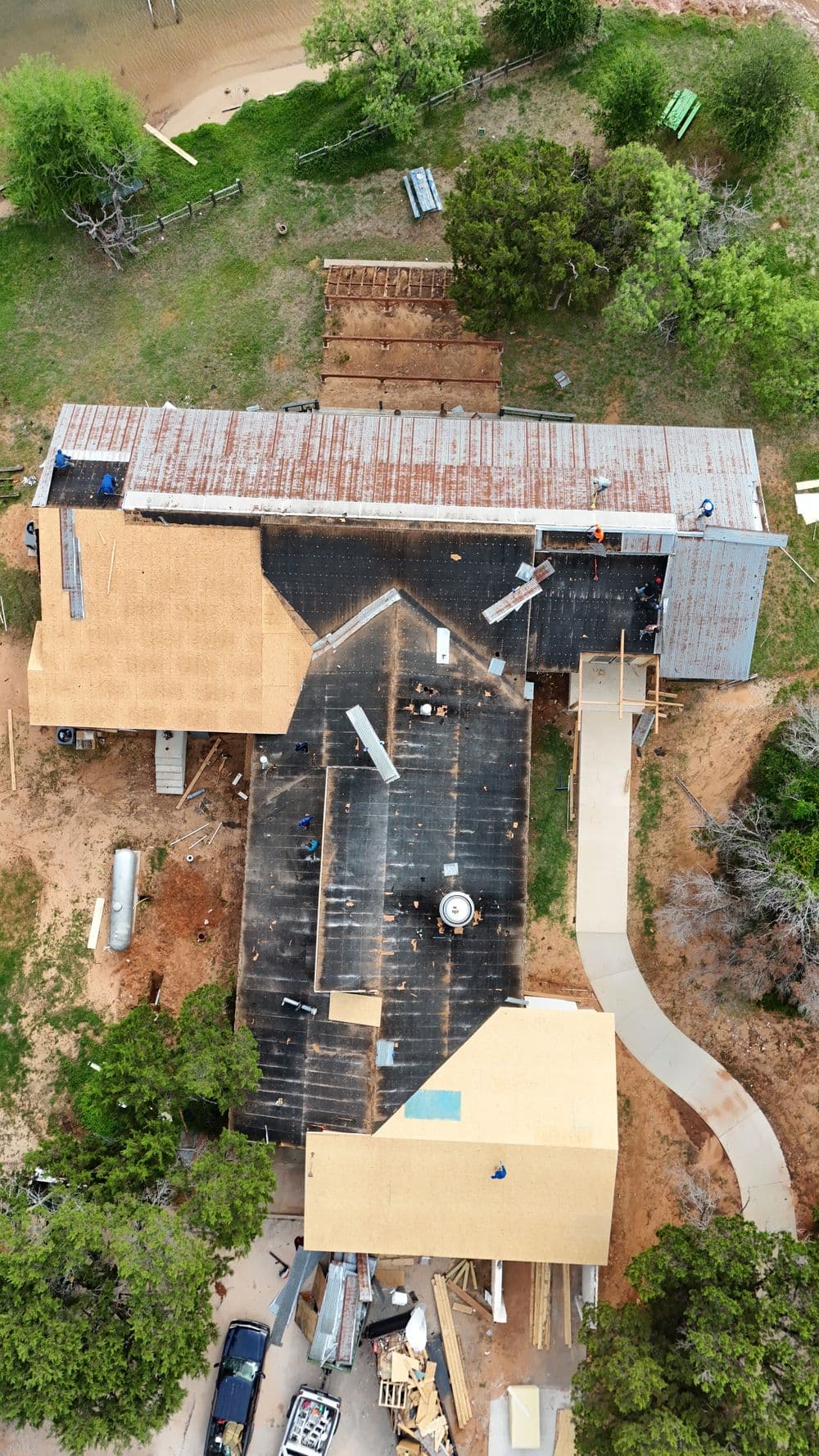 Aerial view of a construction site with roof renovations on two buildings surrounded by trees.