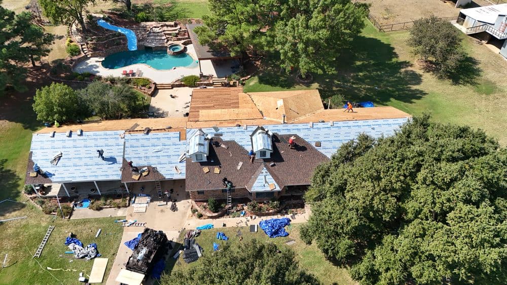 Aerial view of a house undergoing roofing renovations in a spacious backyard with a pool.