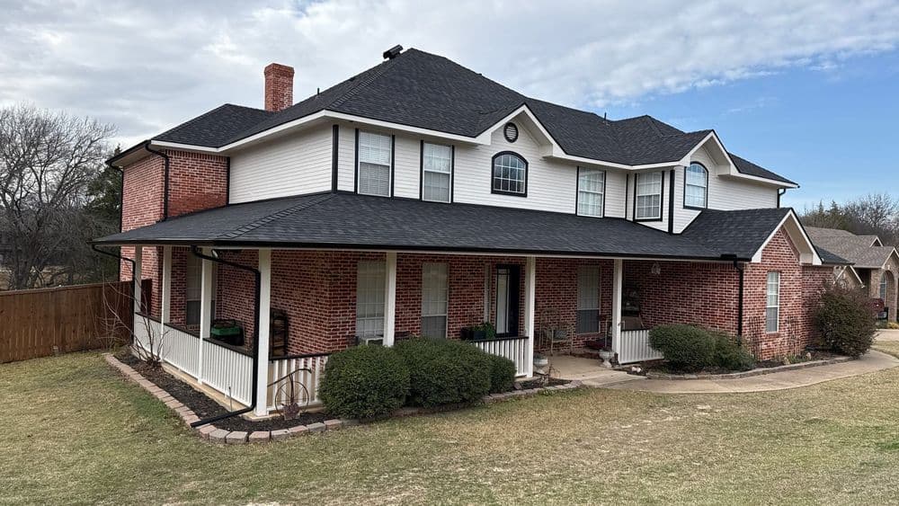 Beautiful red brick house with a wraparound porch and well-maintained lawn under a cloudy sky.
