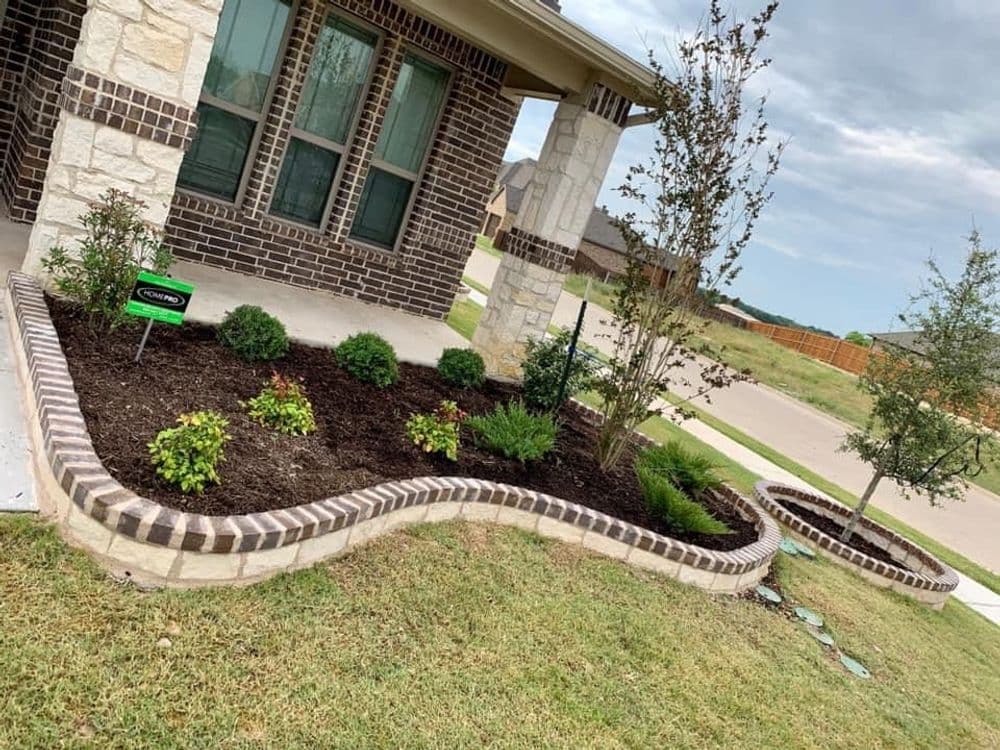 Landscaped flower bed with curved brick edging, featuring bushes and ornamental plants.